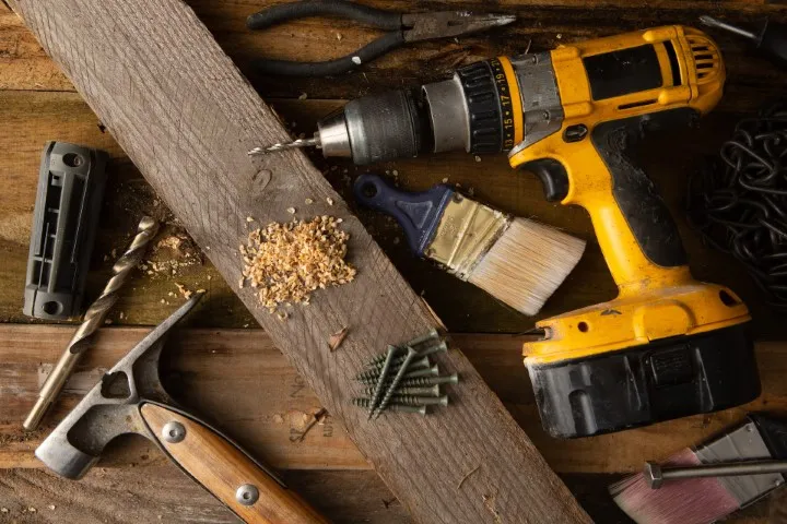 An image showing a yellow power drill, screws and other tool